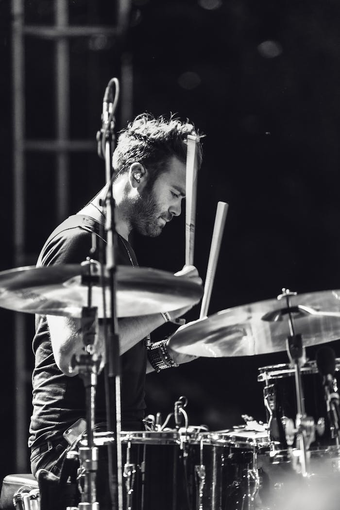 Black and white photo of a drummer performing passionately during a live music concert.