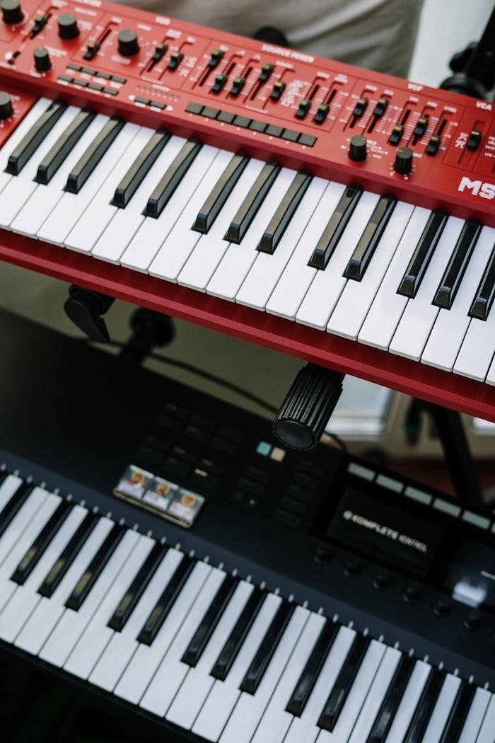 Vertical shot of red and black electronic keyboards in a home studio setting.